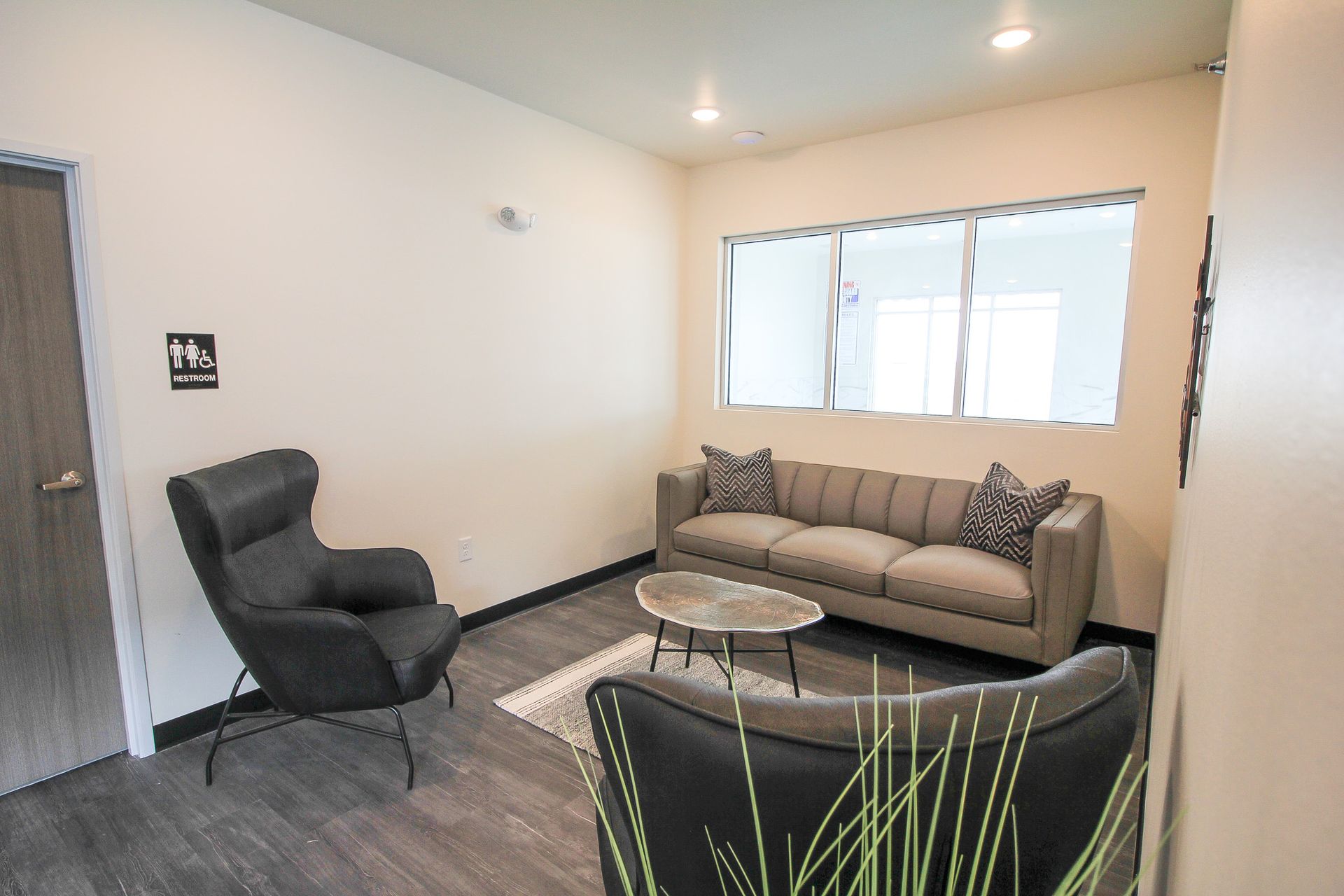 Small living room with gray sofa, black chair, round table, and light walls near a window