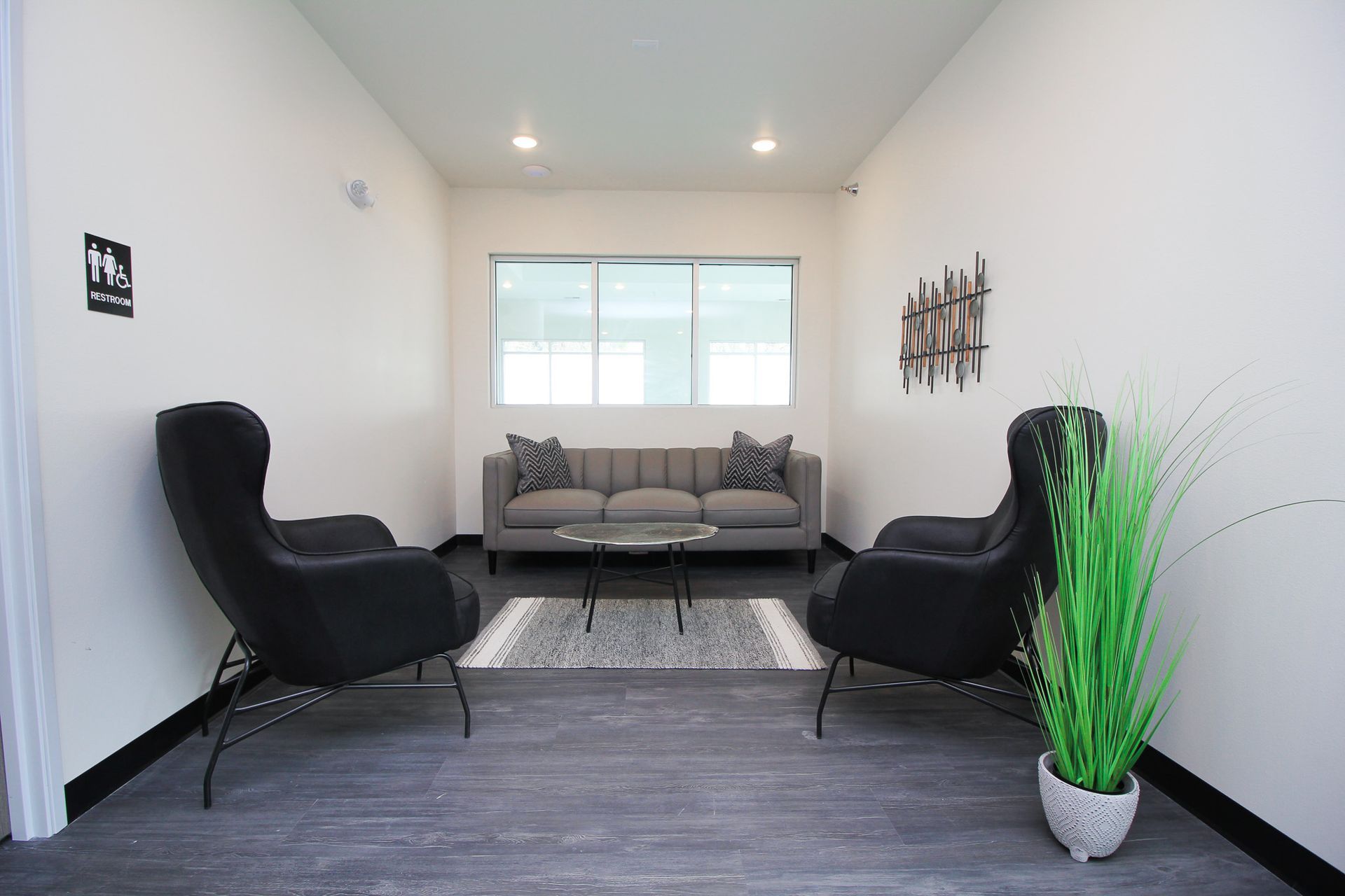 Modern waiting room with gray sofa, black chairs, wall art, and a tall green plant