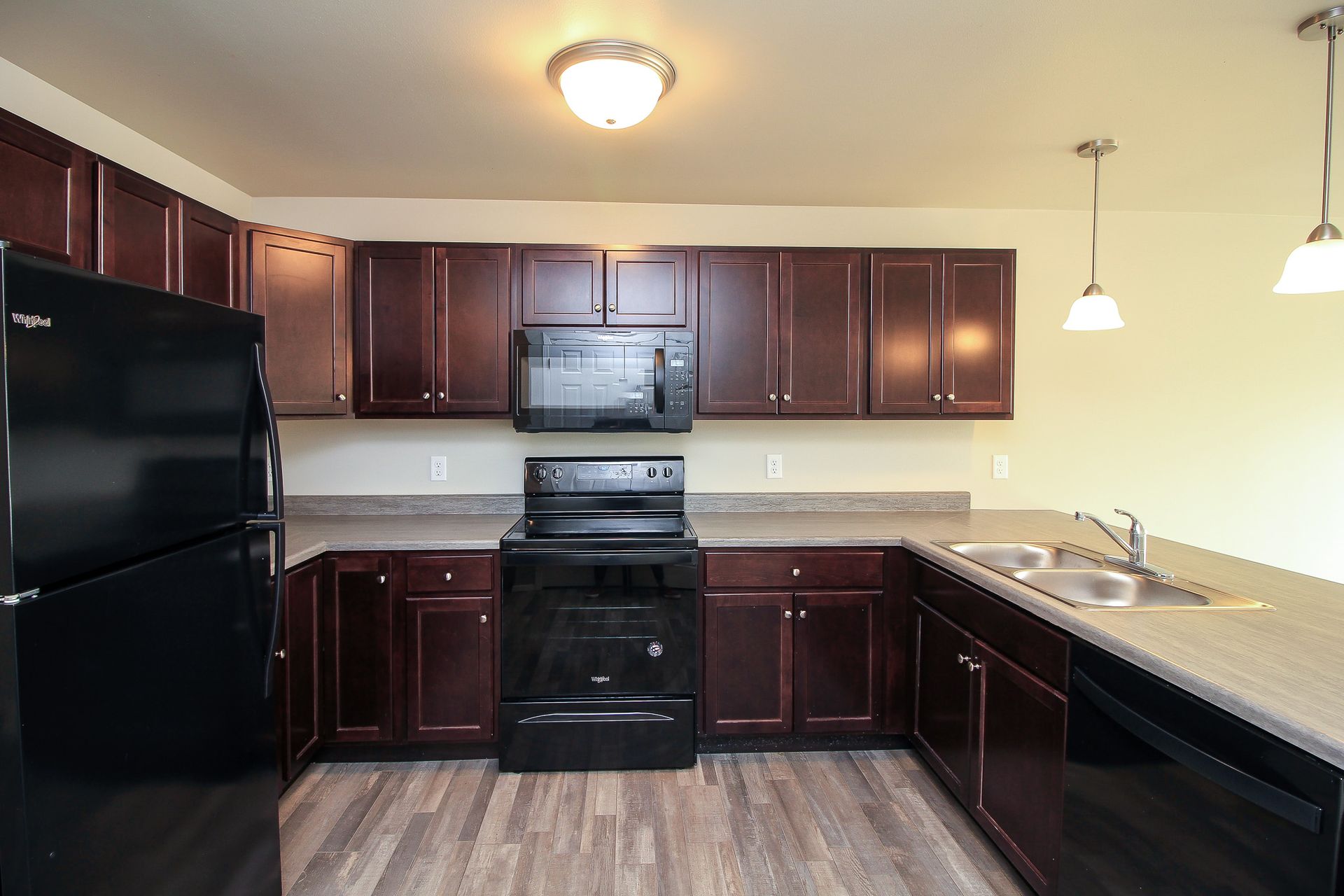 Modern kitchen with dark wood cabinets, black appliances, and a light countertop with sink and pendant lights.