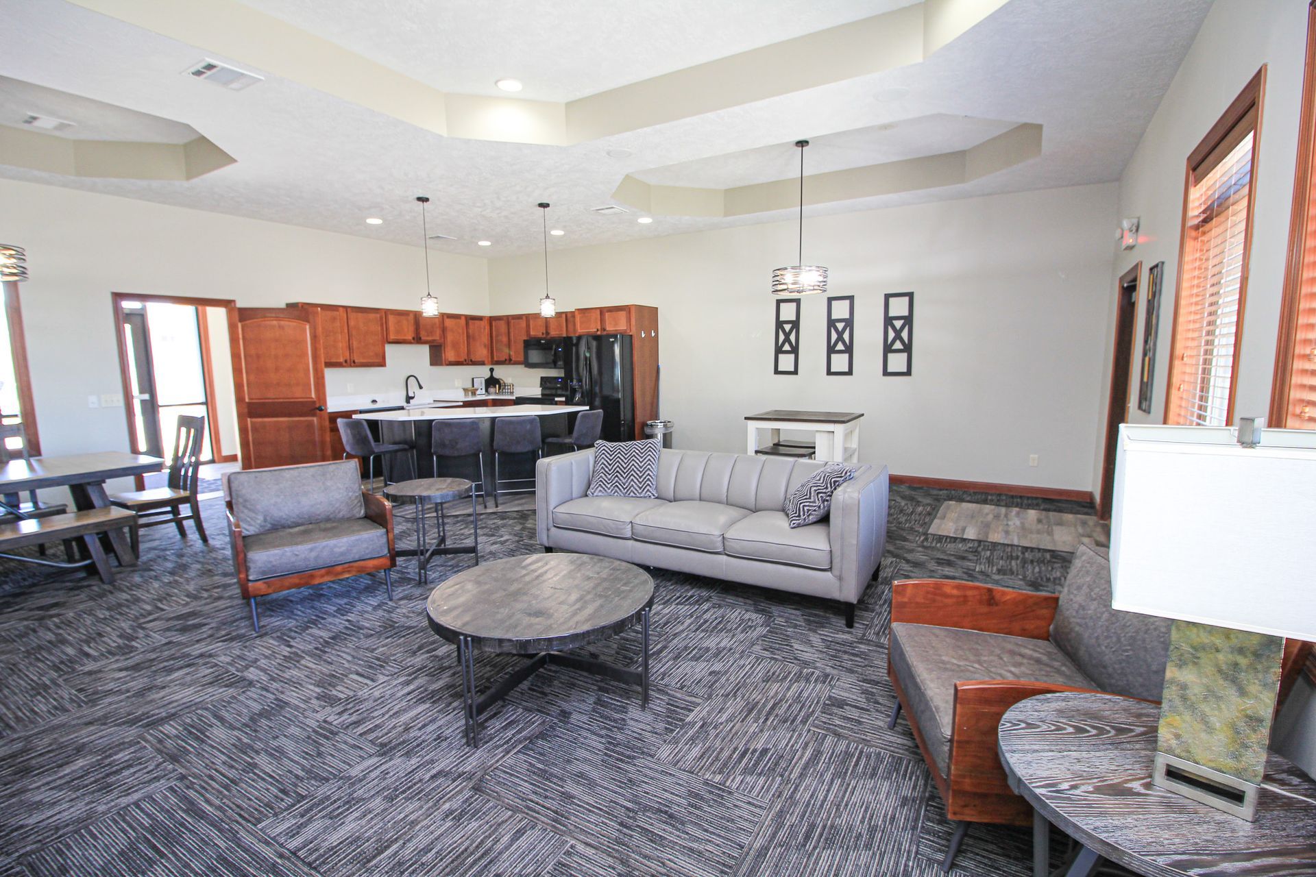 Spacious living room with gray sofa, patterned chairs, coffee table, and open kitchen area