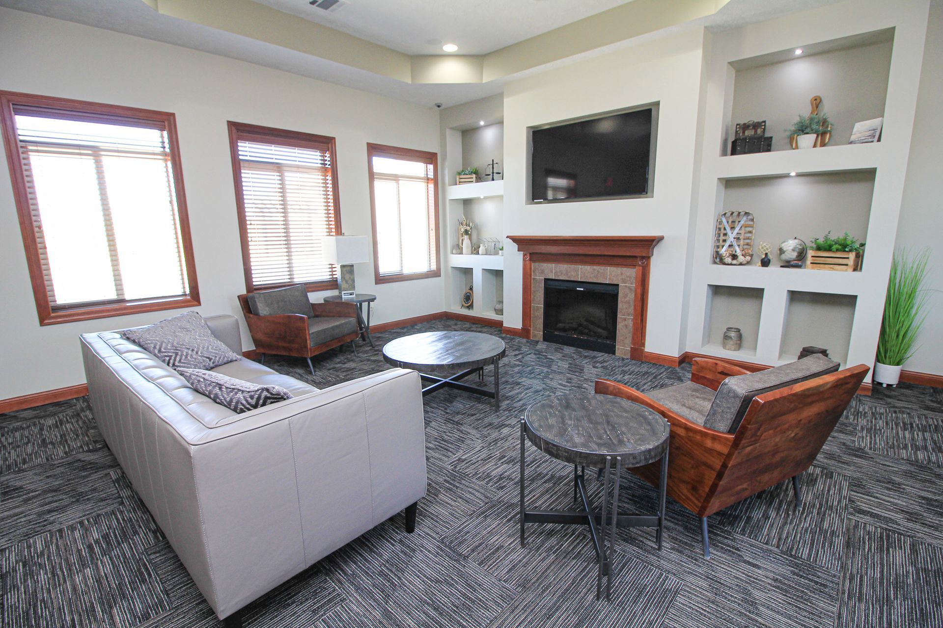 Bright living room with gray sofa, leather chairs, fireplace, wall-mounted TV, and built-in shelves