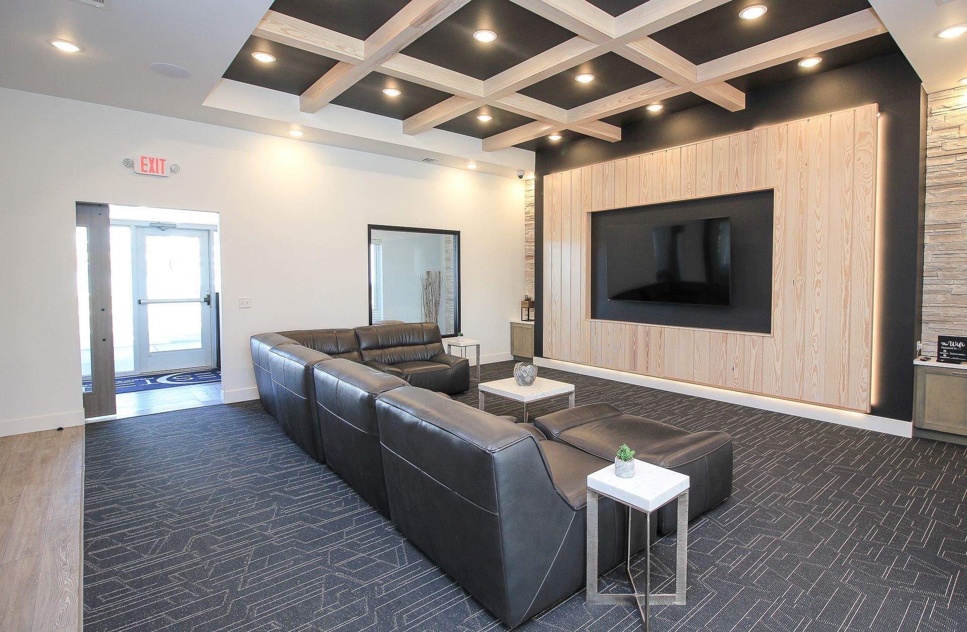 Modern lobby with black leather seating, patterned carpet, wall-mounted TV, and ceiling lights