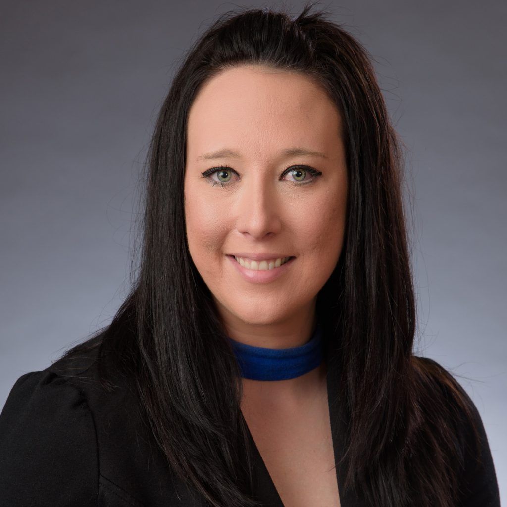 Portrait of a smiling woman with long dark hair wearing a black top and blue choker on a gray background