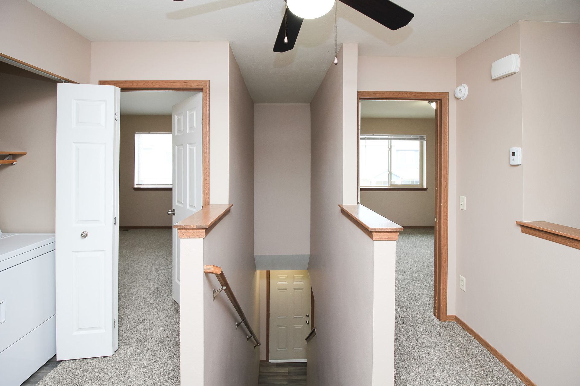 Interior hallway with beige walls, carpet, white doors, and a stairwell opening in the center.