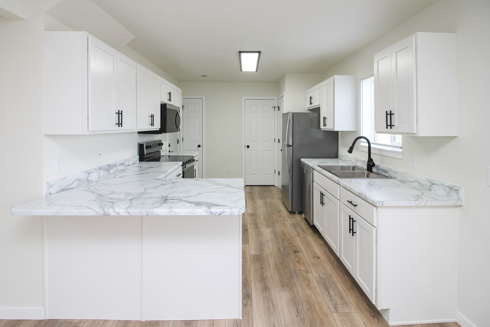 Bright modern kitchen with white cabinets, marble countertops, and wood flooring