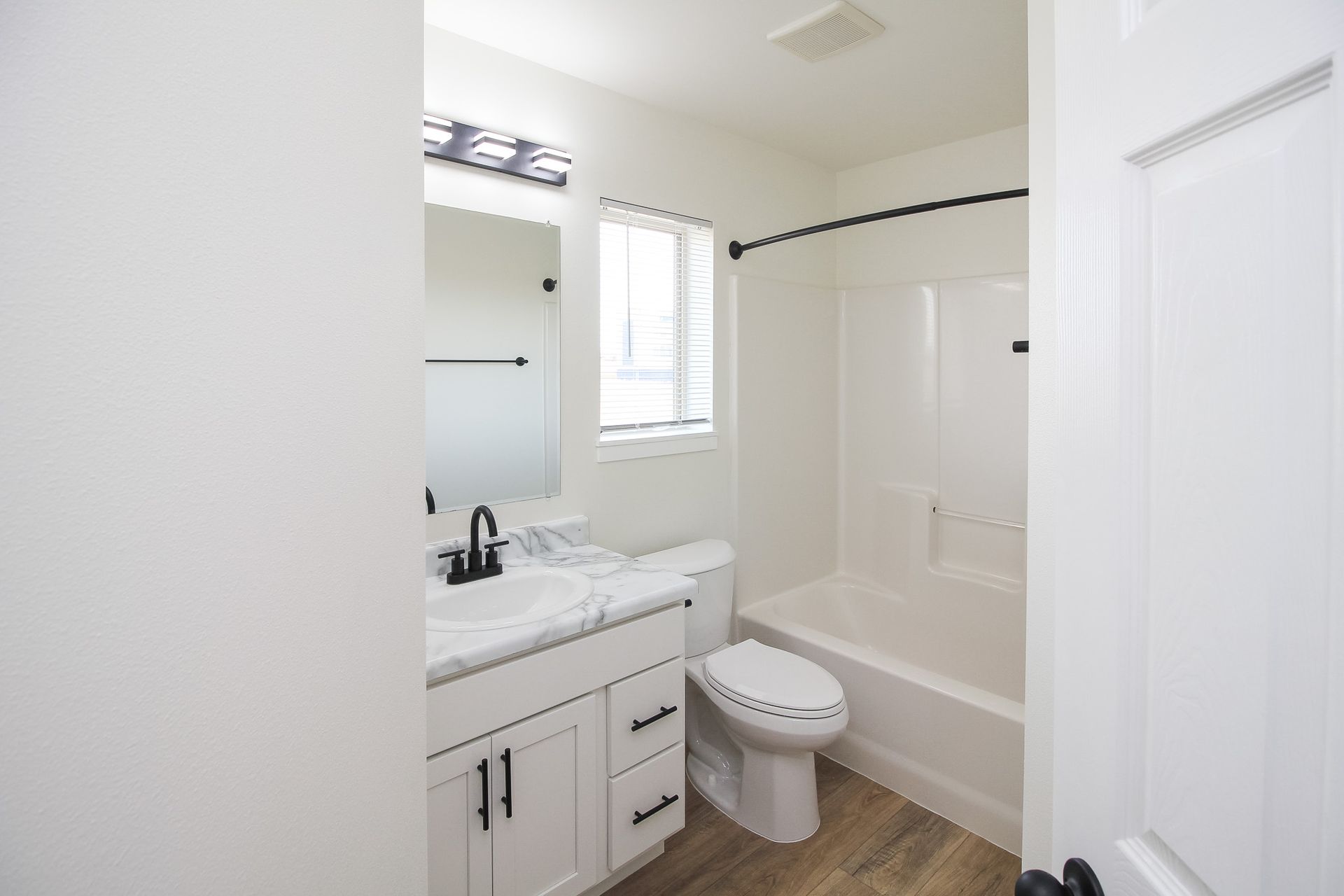 Small white bathroom with vanity, toilet, shower-tub combo, and window.
