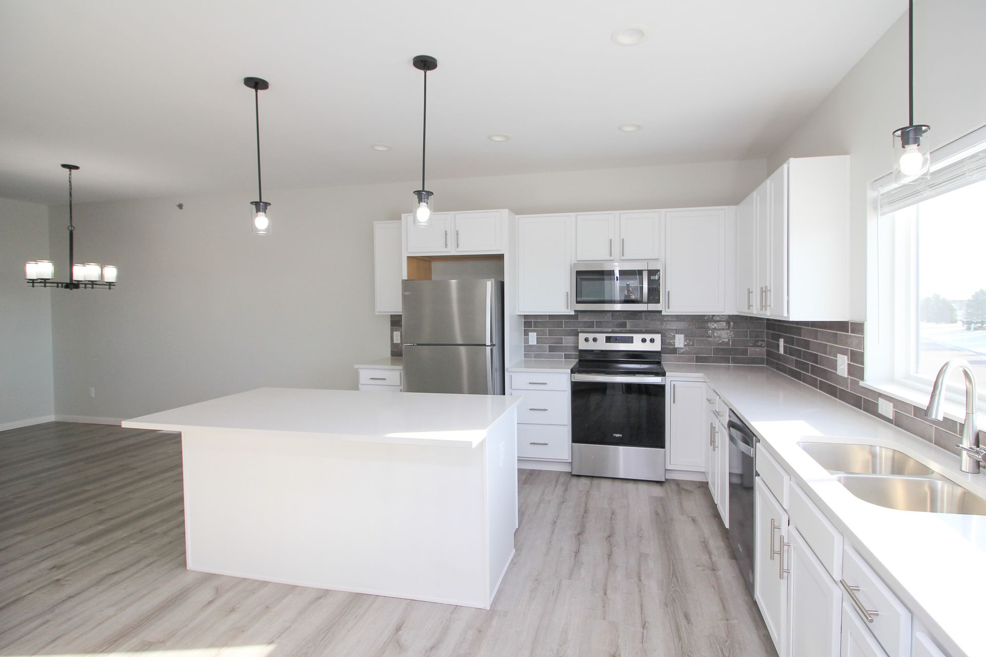 Bright modern kitchen with white cabinets, island, stainless steel appliances, and large windows
