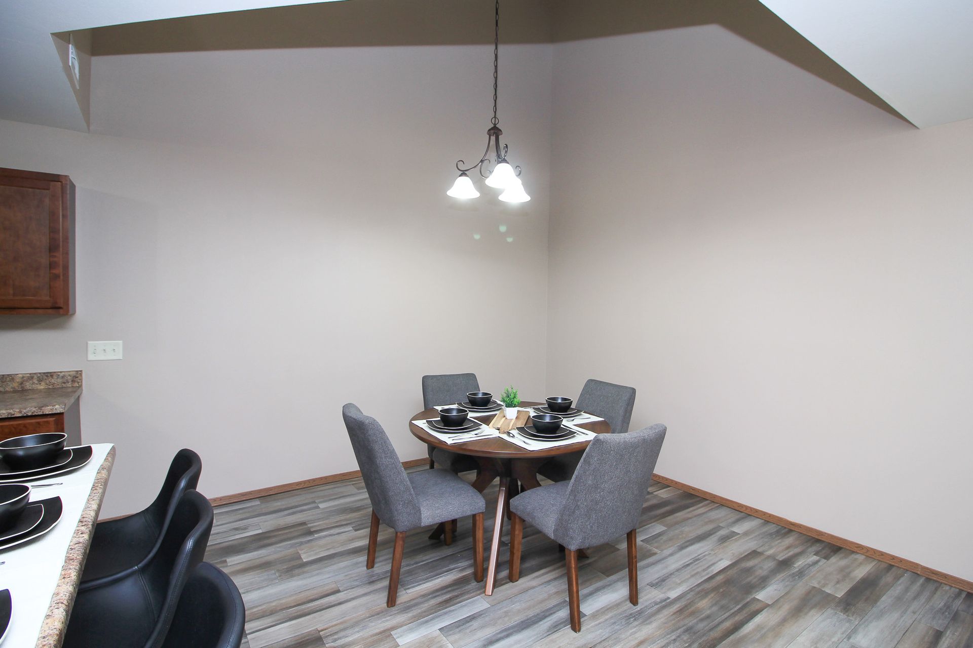 Dining area with round table, four gray chairs, and hanging light in a mostly empty kitchen.