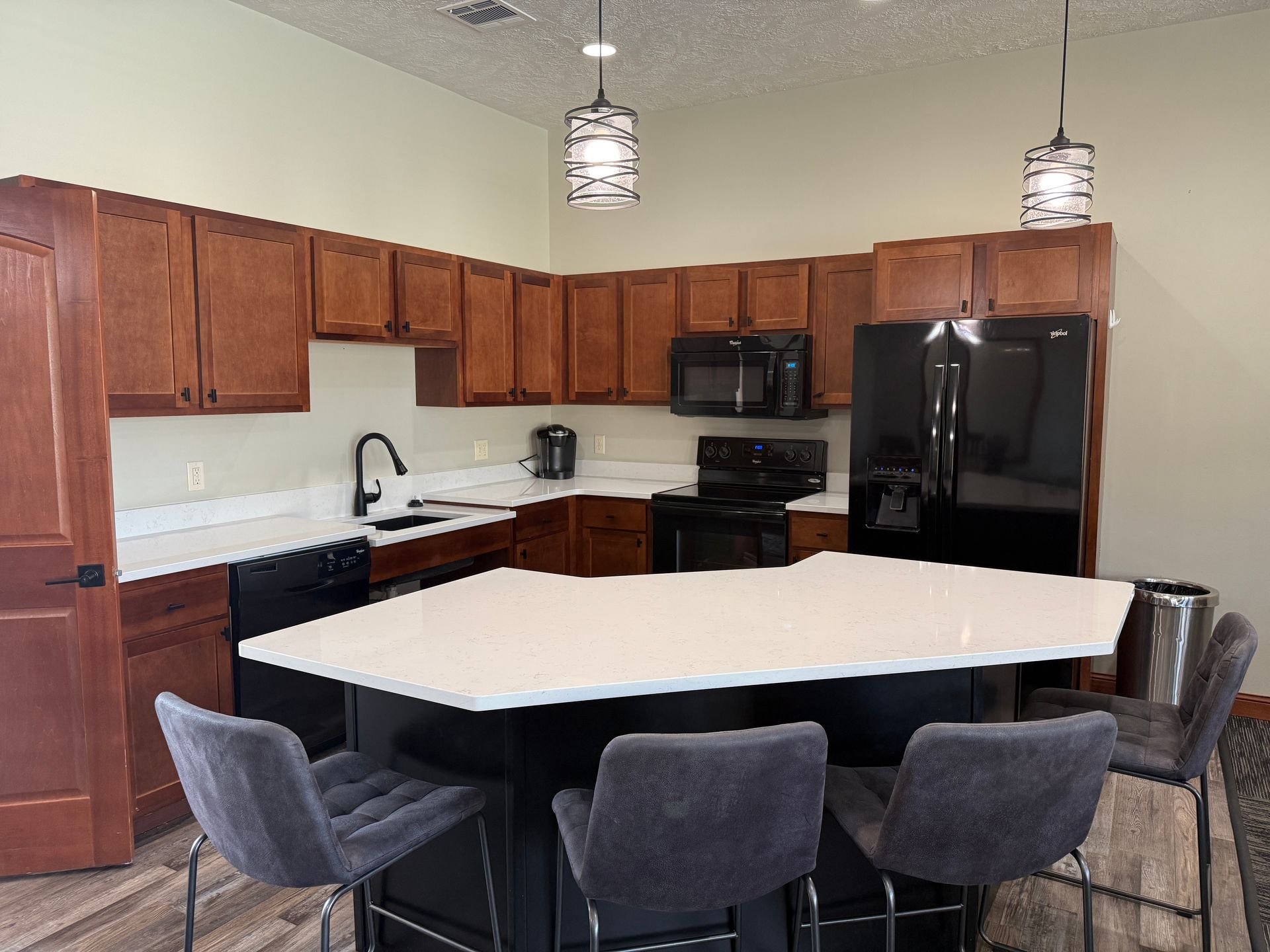 Modern kitchen with dark wood cabinets, black appliances, and a white island with stools