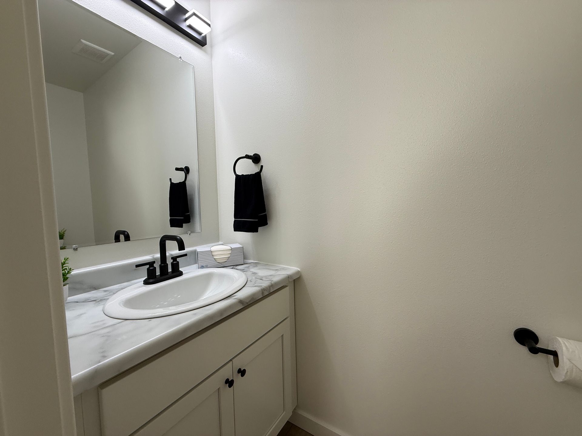 Bathroom vanity with sink, mirror, white cabinet, and towel ring on a beige wall.