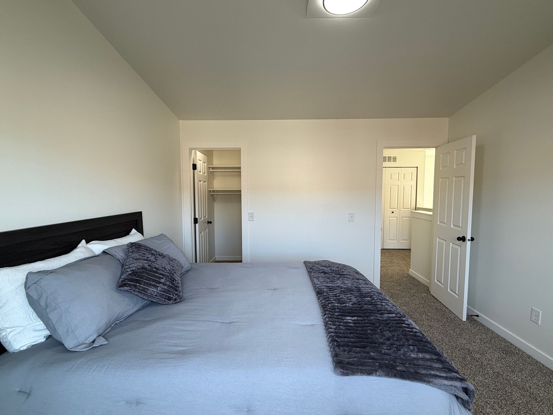Bright bedroom with a bed, gray bedding, and open doors to a closet and hallway.
