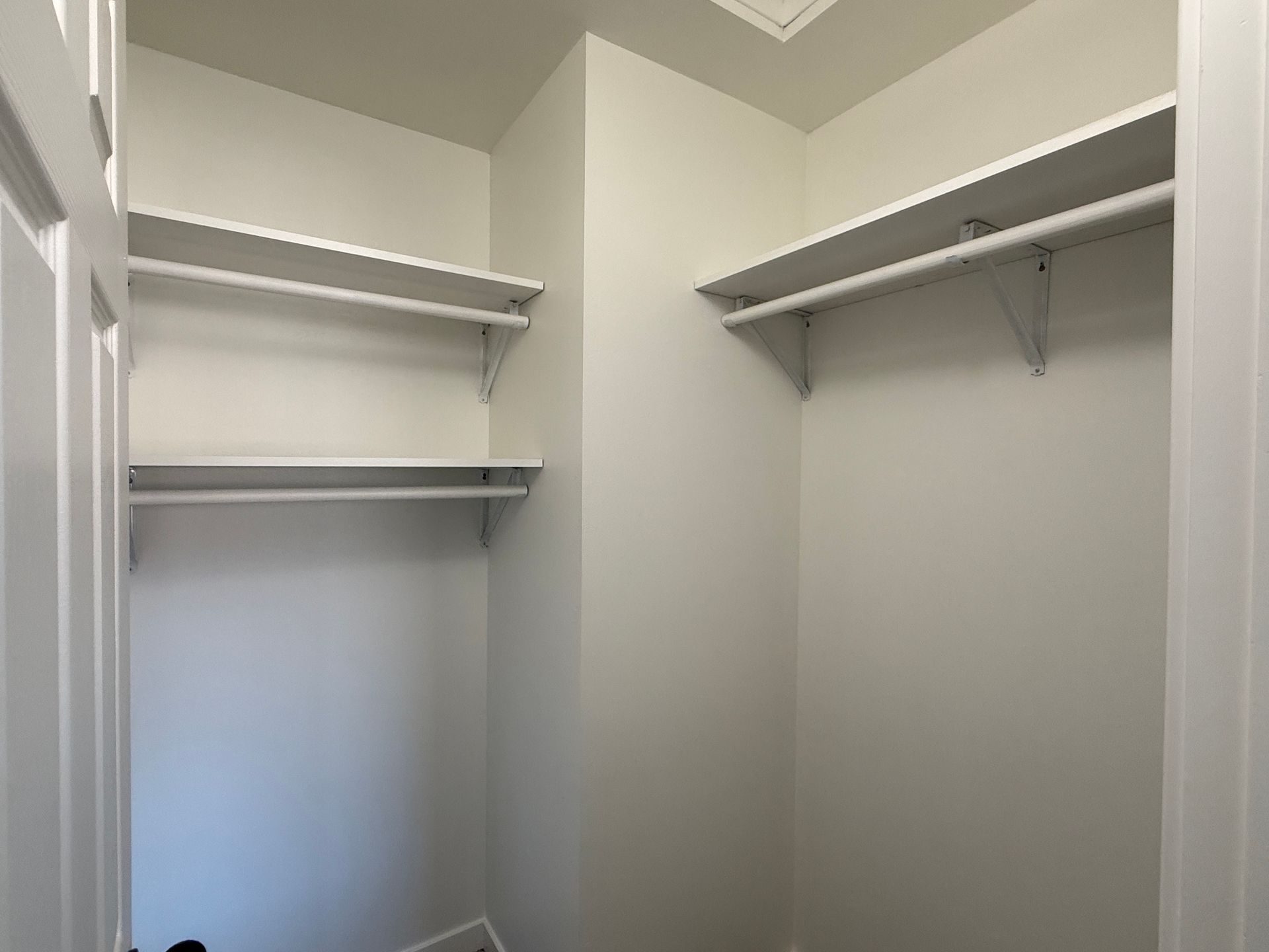 Empty walk-in closet with white shelves and hanging rods on light gray walls