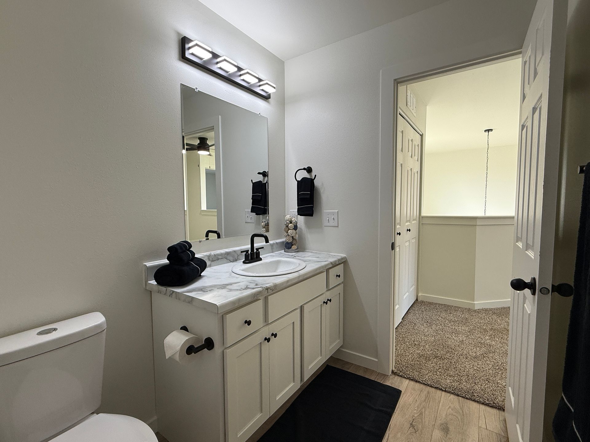 Bright bathroom with vanity, mirror, toilet, and doorway to carpeted hall