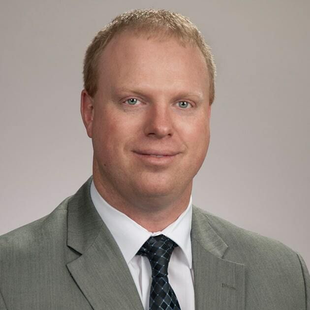 Studio headshot of a man in a gray suit and patterned tie, against a neutral background