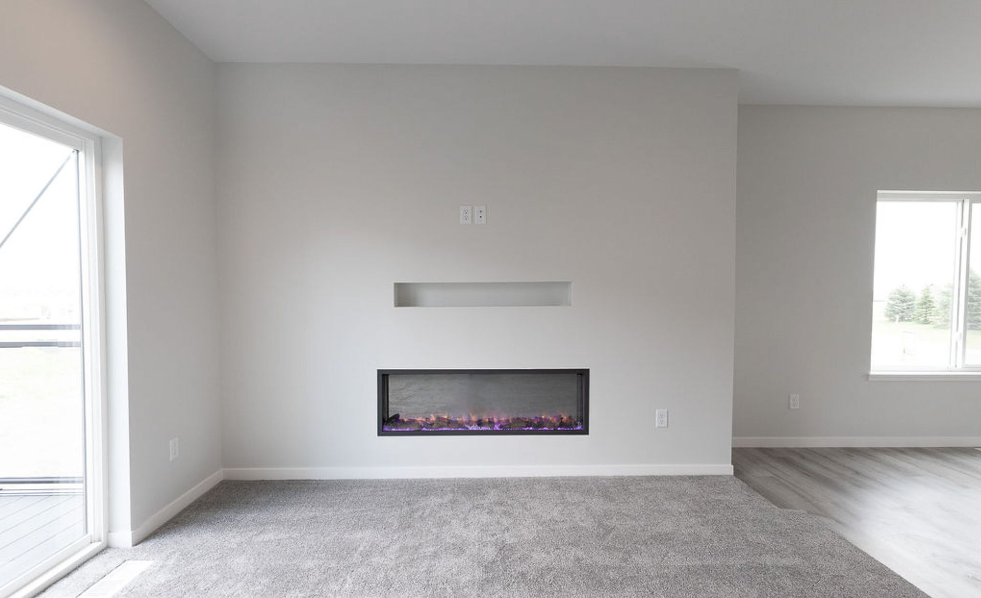 Empty living room with gray carpet, light walls, a modern fireplace, and sliding glass door.