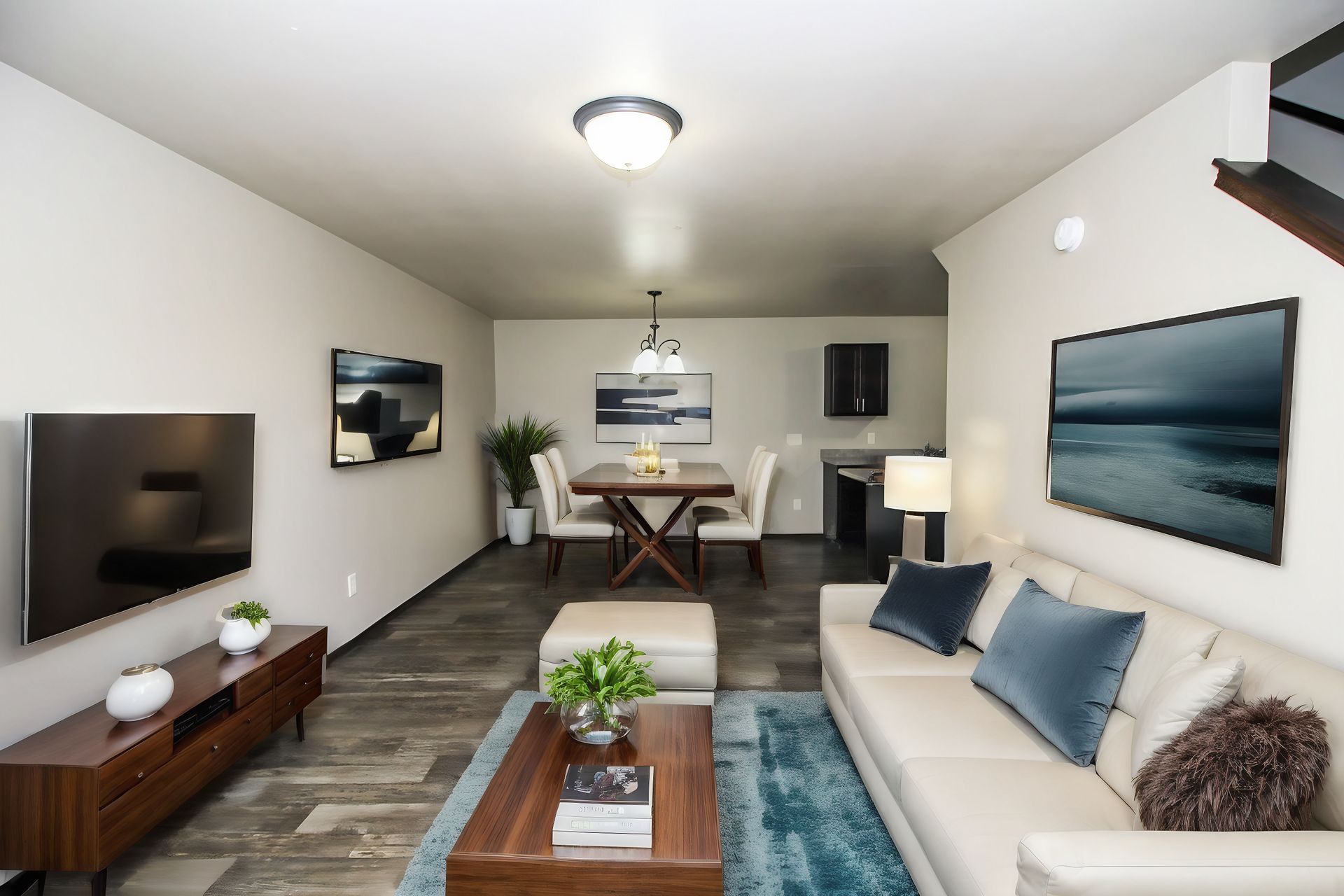 Modern living room with white sofa, wall-mounted TV, coffee table, and dining area in the background