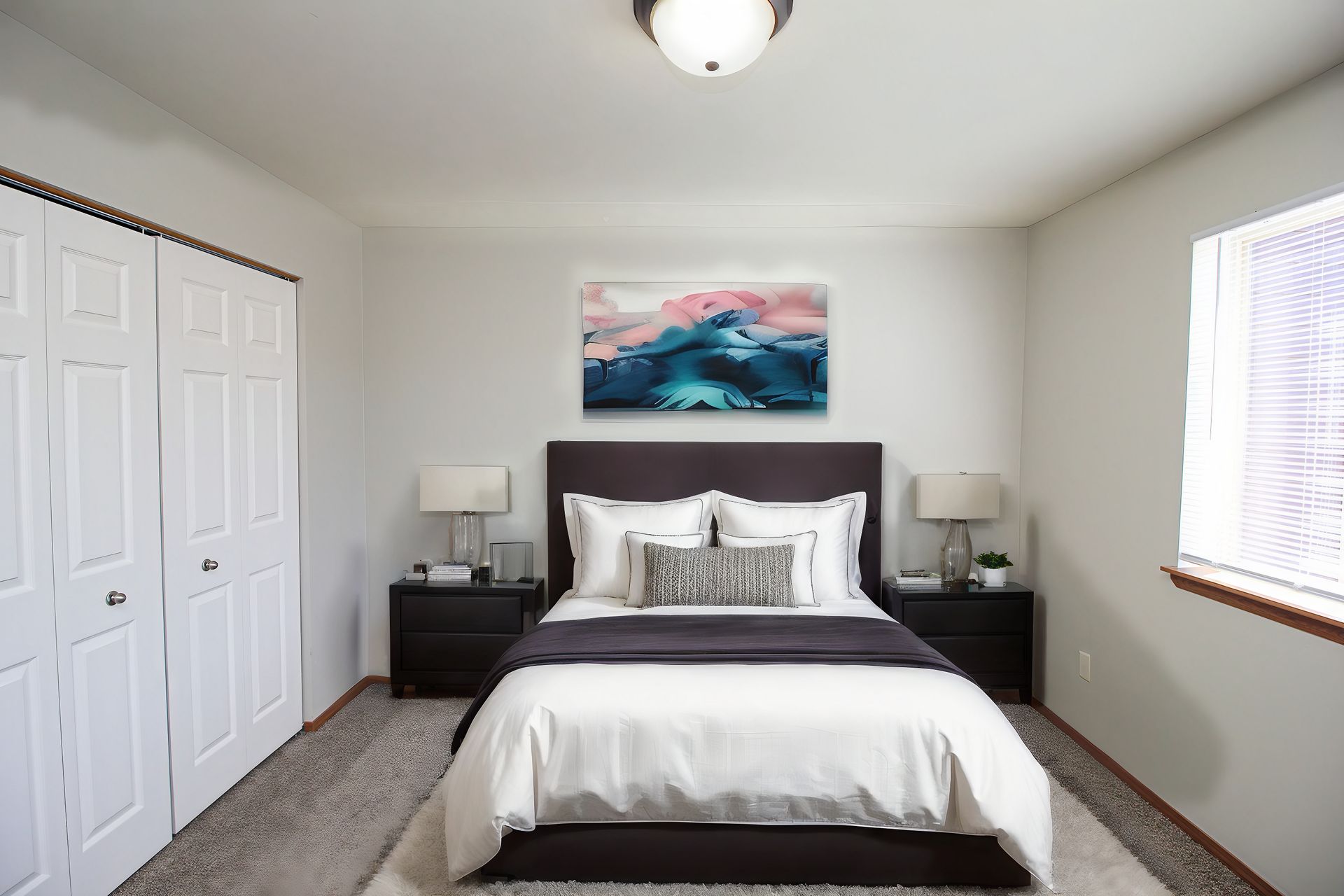 Bright bedroom with a dark bed, white bedding, nightstands, and a colorful ocean painting above the headboard