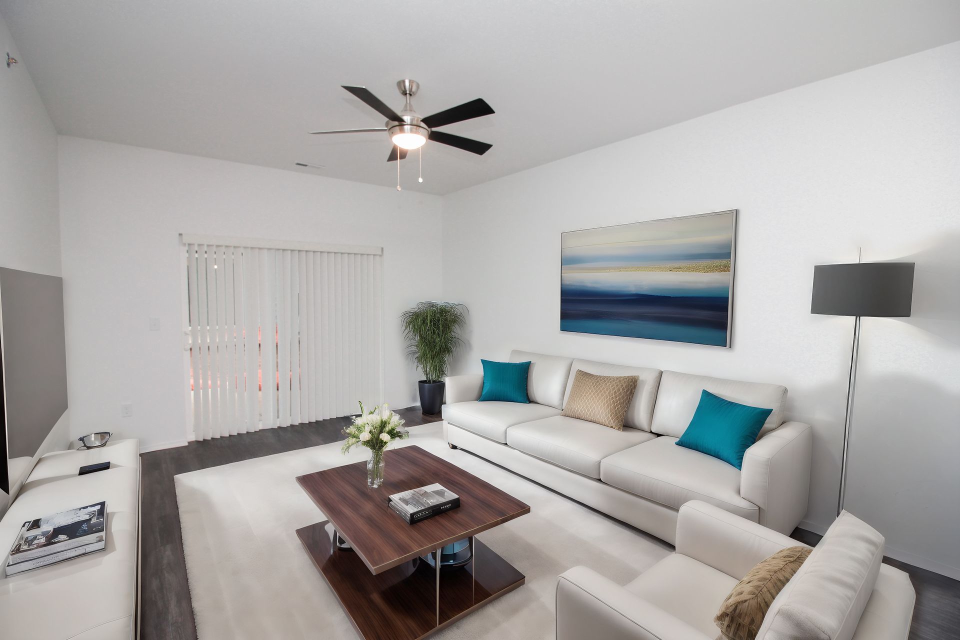 Bright modern living room with white sofa, coffee table, floor lamp, wall art, and ceiling fan.