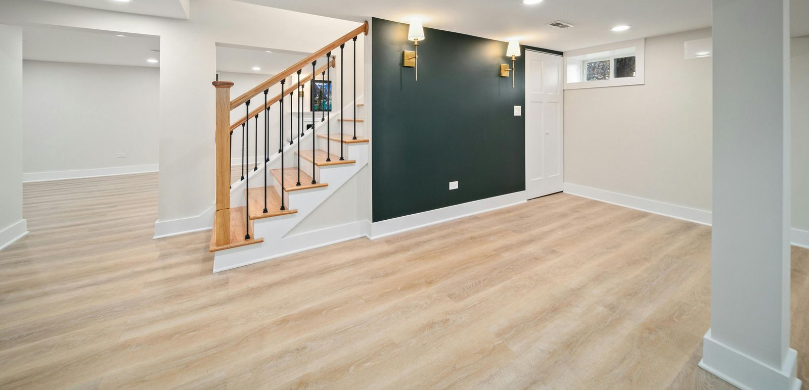 Empty modern living room with light wood floors, white walls, and a staircase with wooden handrail.