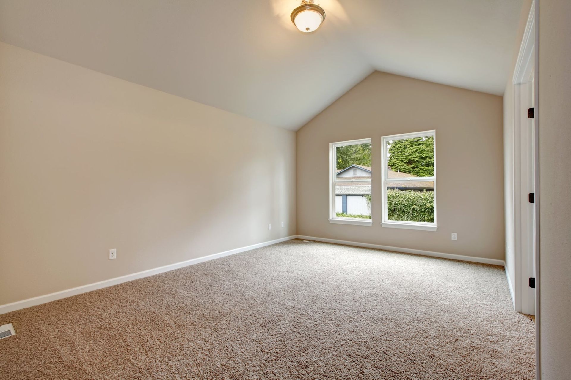 Empty beige carpeted bedroom with vaulted ceiling and a window letting in natural light