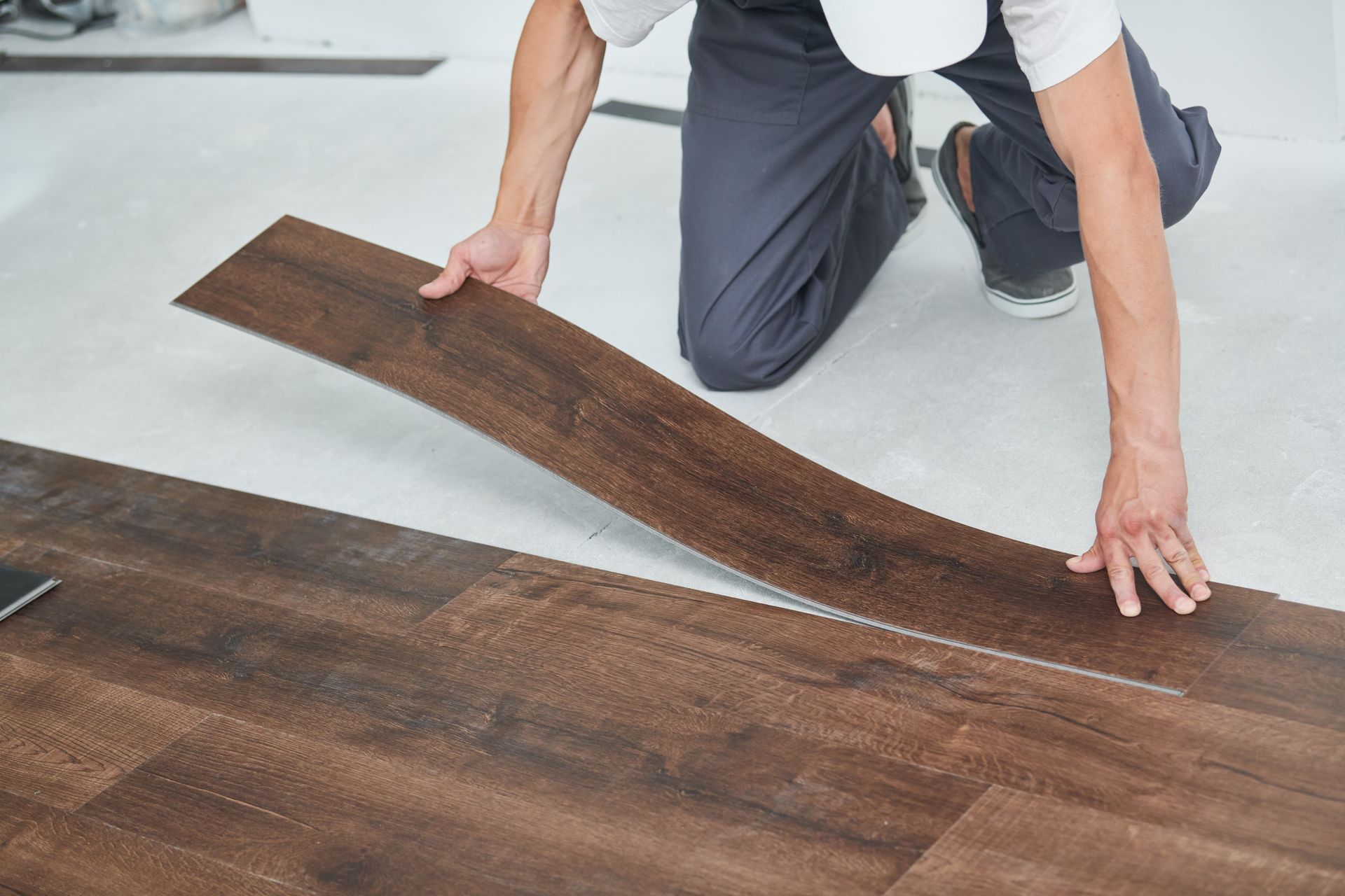 Person kneeling on a white floor, fitting dark wood planks into place.