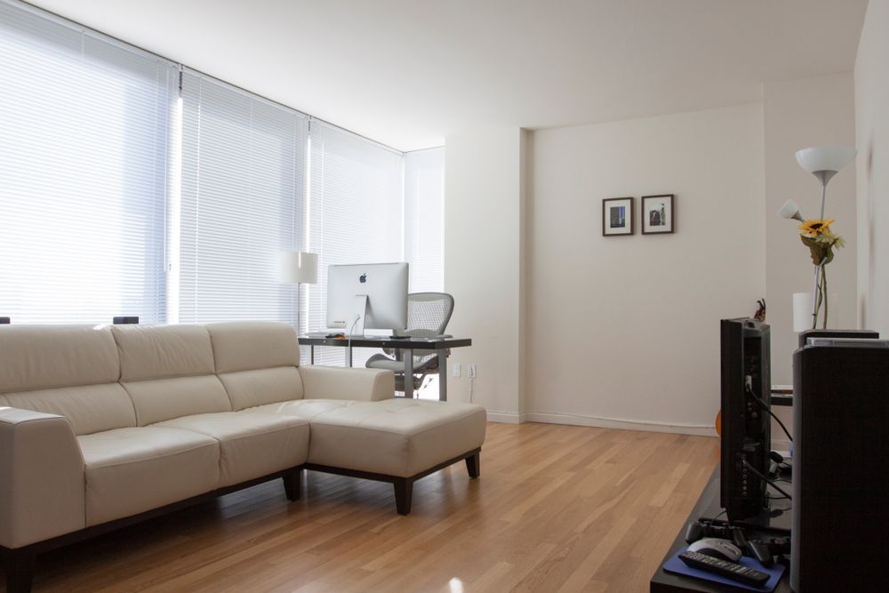 Bright living room with beige sectional sofa, hardwood floors, and a desk by large windows.