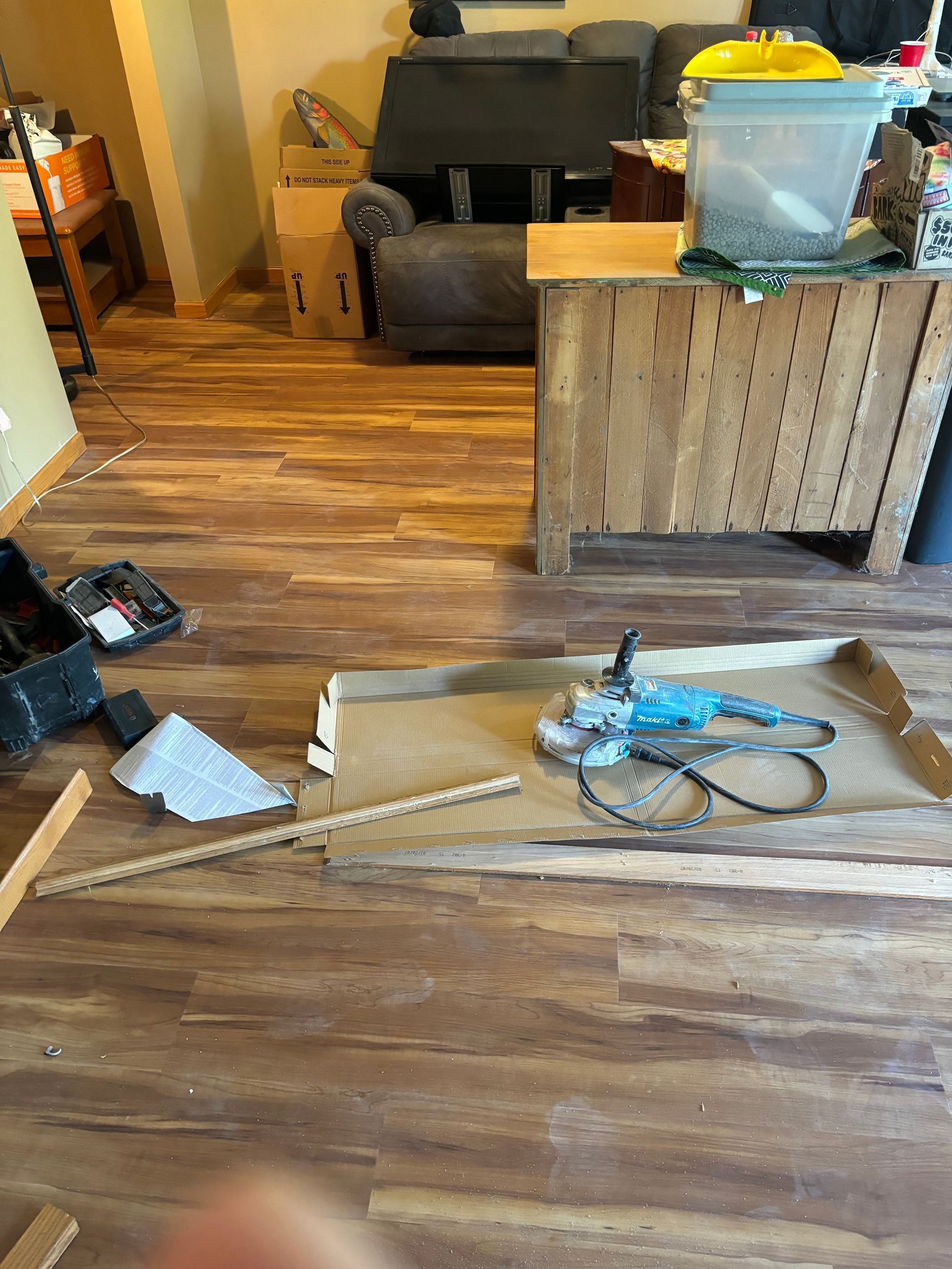 Cluttered living room with scattered tools and boxes on a wood floor near a couch and wooden cabinet