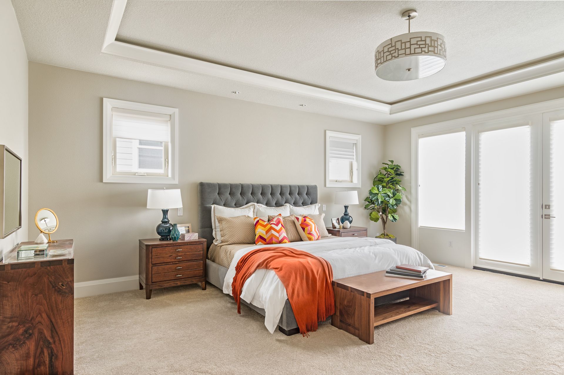 Bright bedroom with tufted bed, orange accents, bedside tables, and large windows