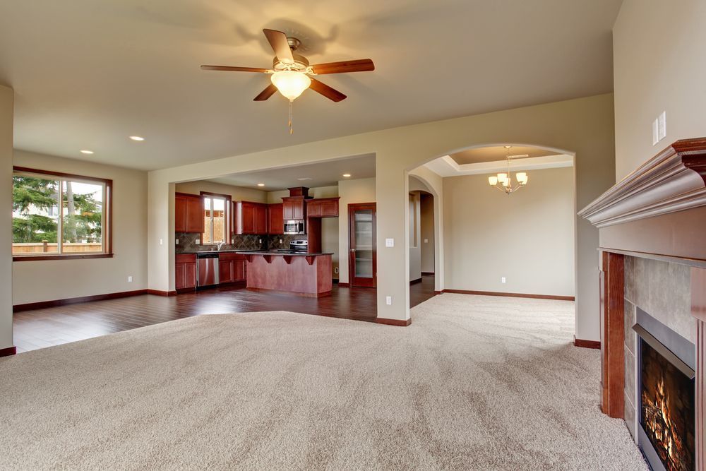 Spacious living room with carpet, fireplace, ceiling fan, and open view into the kitchen