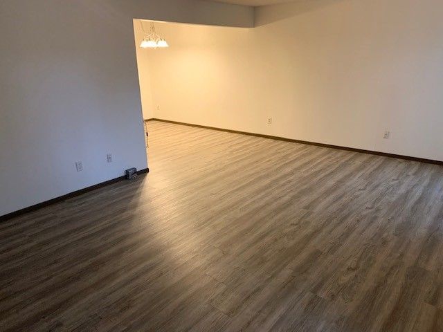 Empty room with wood flooring, white walls, and an open doorway leading to a lit adjacent space.