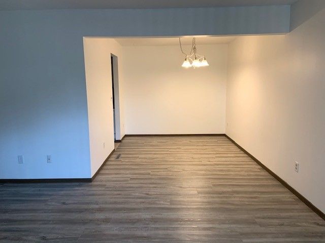 Empty dining room with wood-look flooring, white walls, and a hanging light fixture