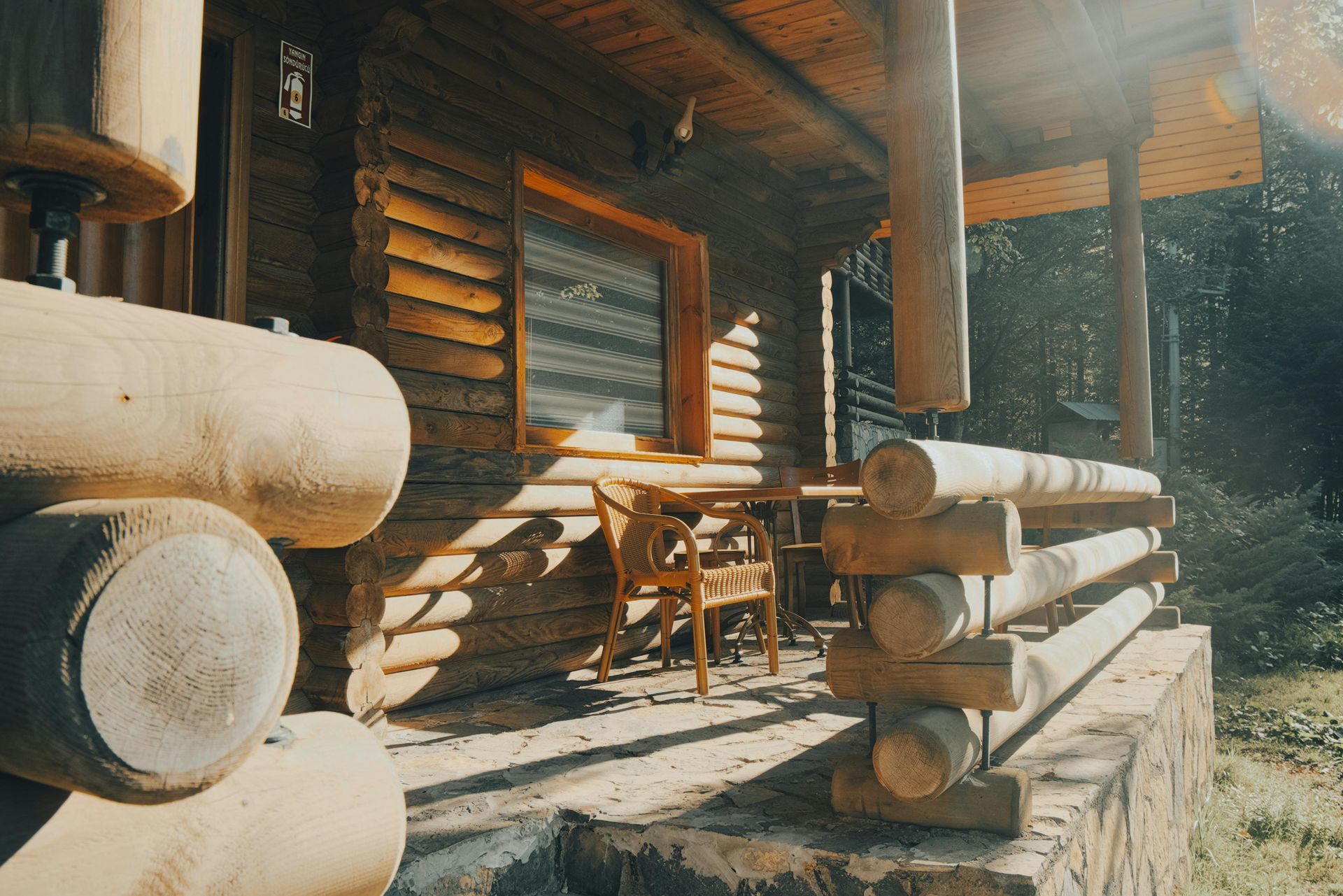 Log cabin porch with stacked logs, wooden chairs, and a table in warm sunlight