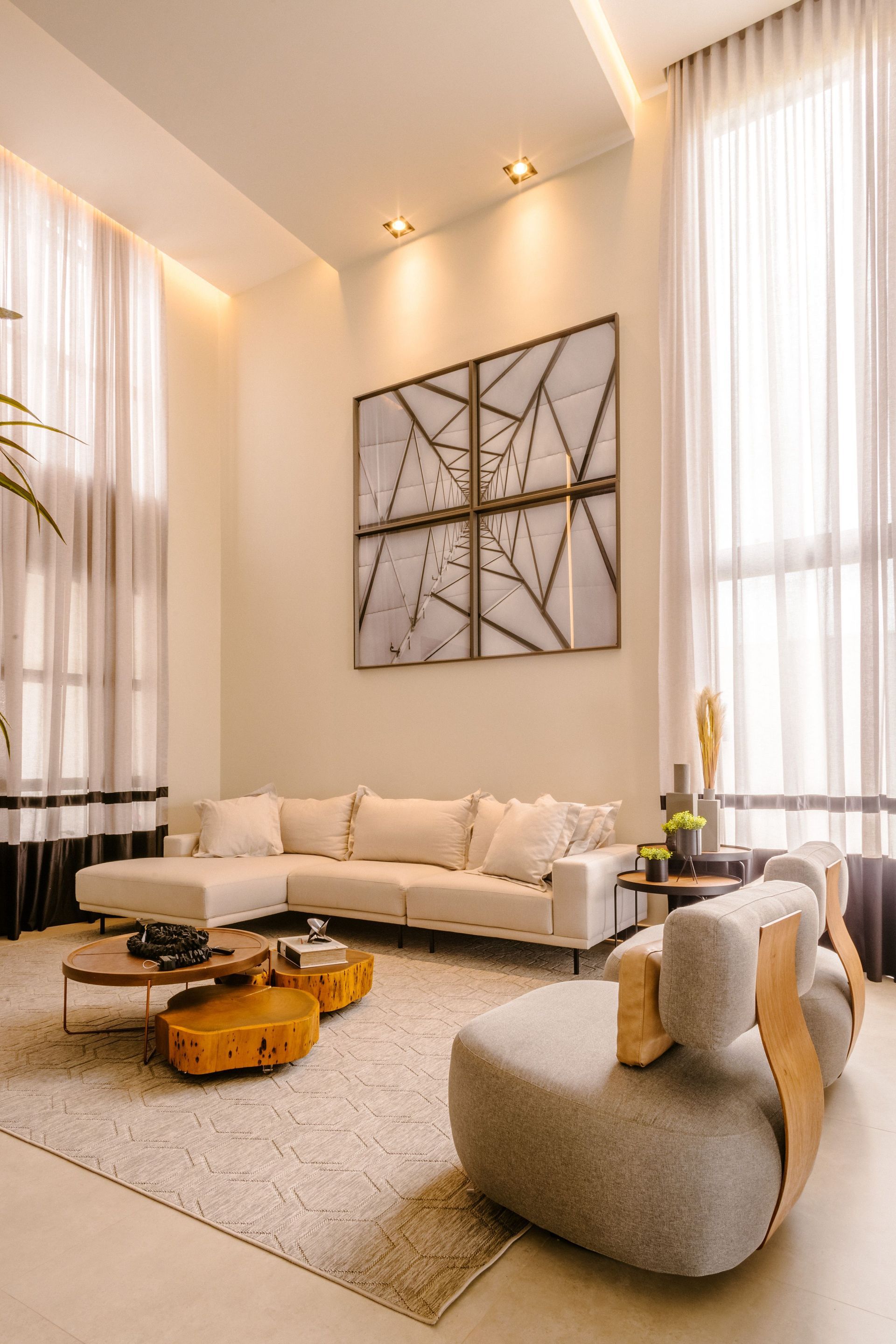Bright modern living room with tall windows, beige sofa, gray chair, rug, and geometric wall art.