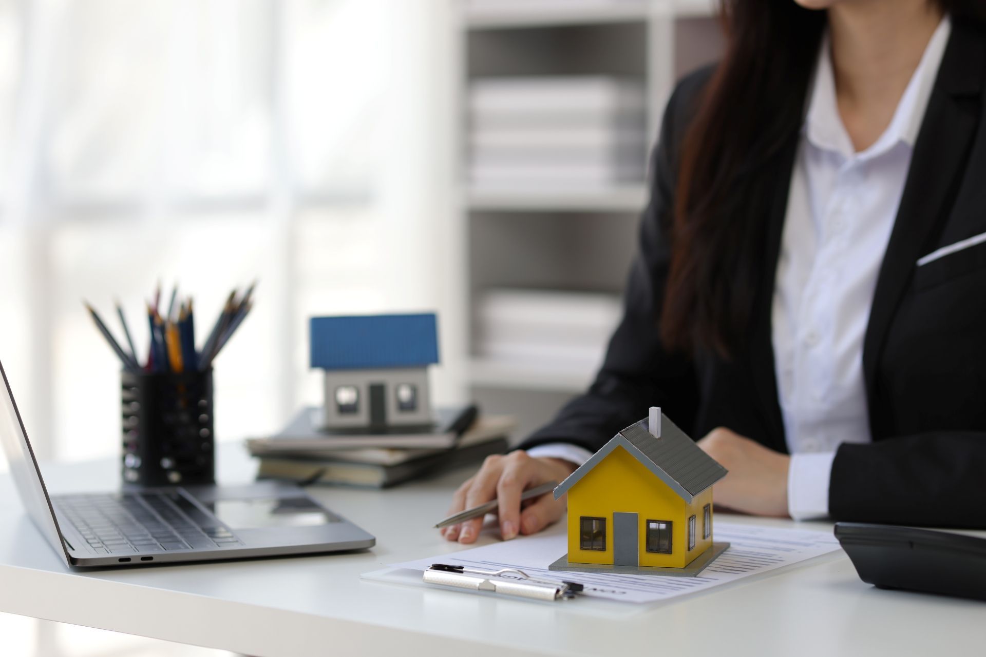 Businesswoman at desk with laptop, pen, and miniature house model in office setting