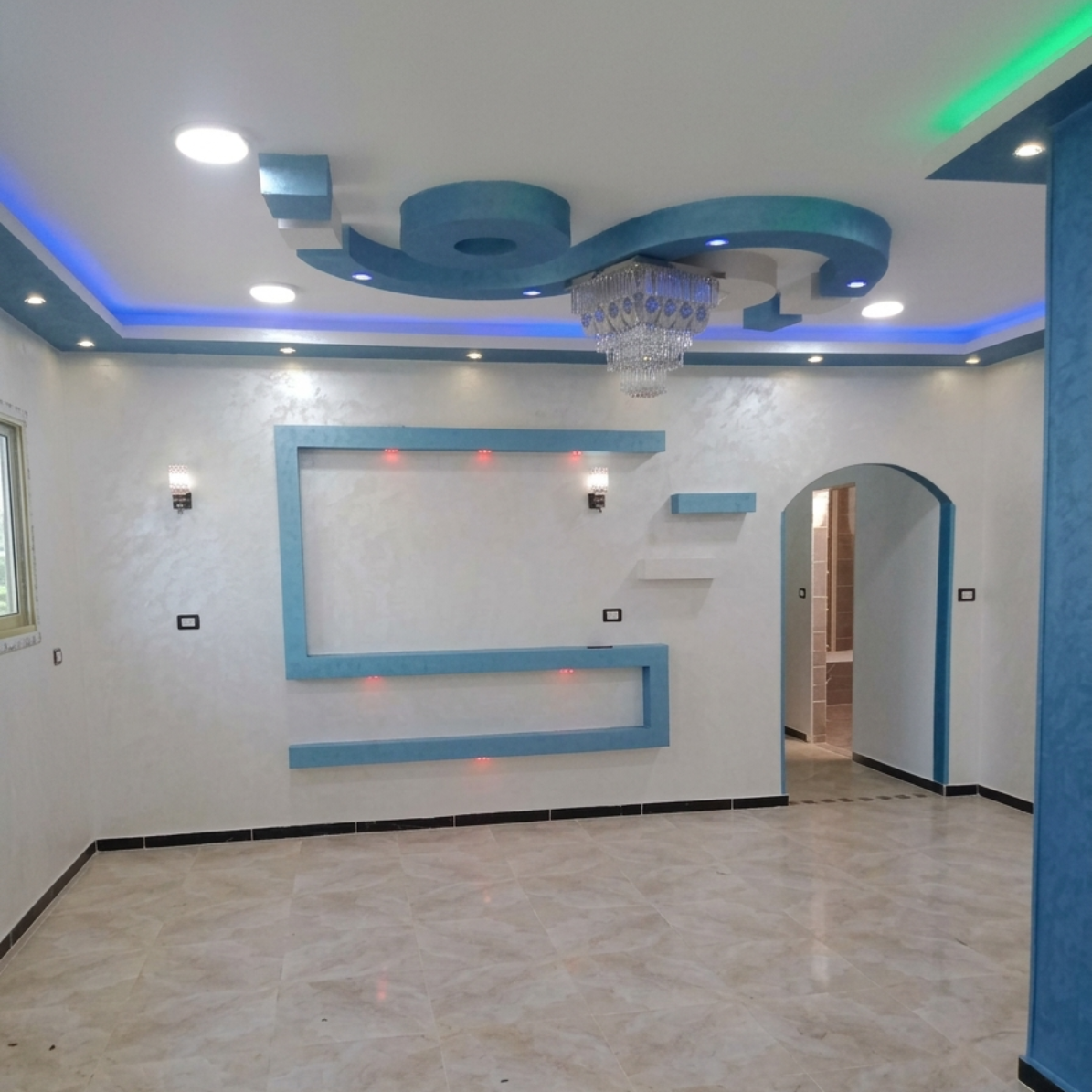Un soggiorno moderno con soffitto a cassettoni blu e bianco, una nicchia decorativa a muro blu e un lampadario di cristallo.