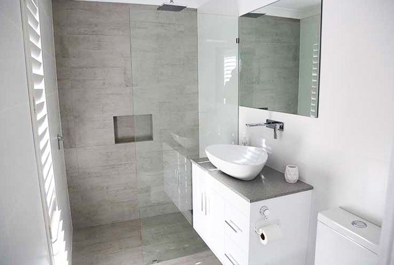 Modern bathroom with a white vanity, vessel sink, walk-in shower with grey tile walls, and a toilet.