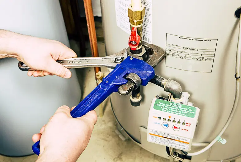 A person uses an adjustable wrench and a blue pipe wrench to tighten a valve on a water heater.