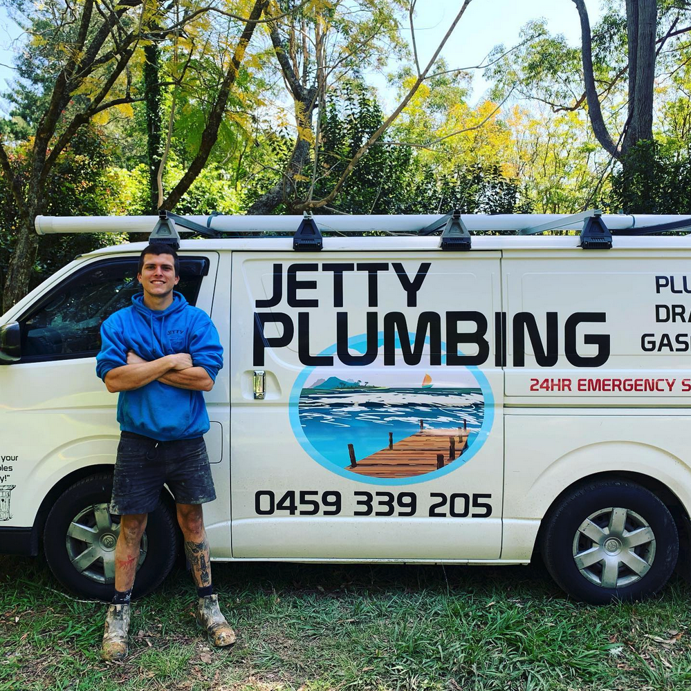 A plumber stands with arms crossed in front of a white van branded with Jetty Plumbing