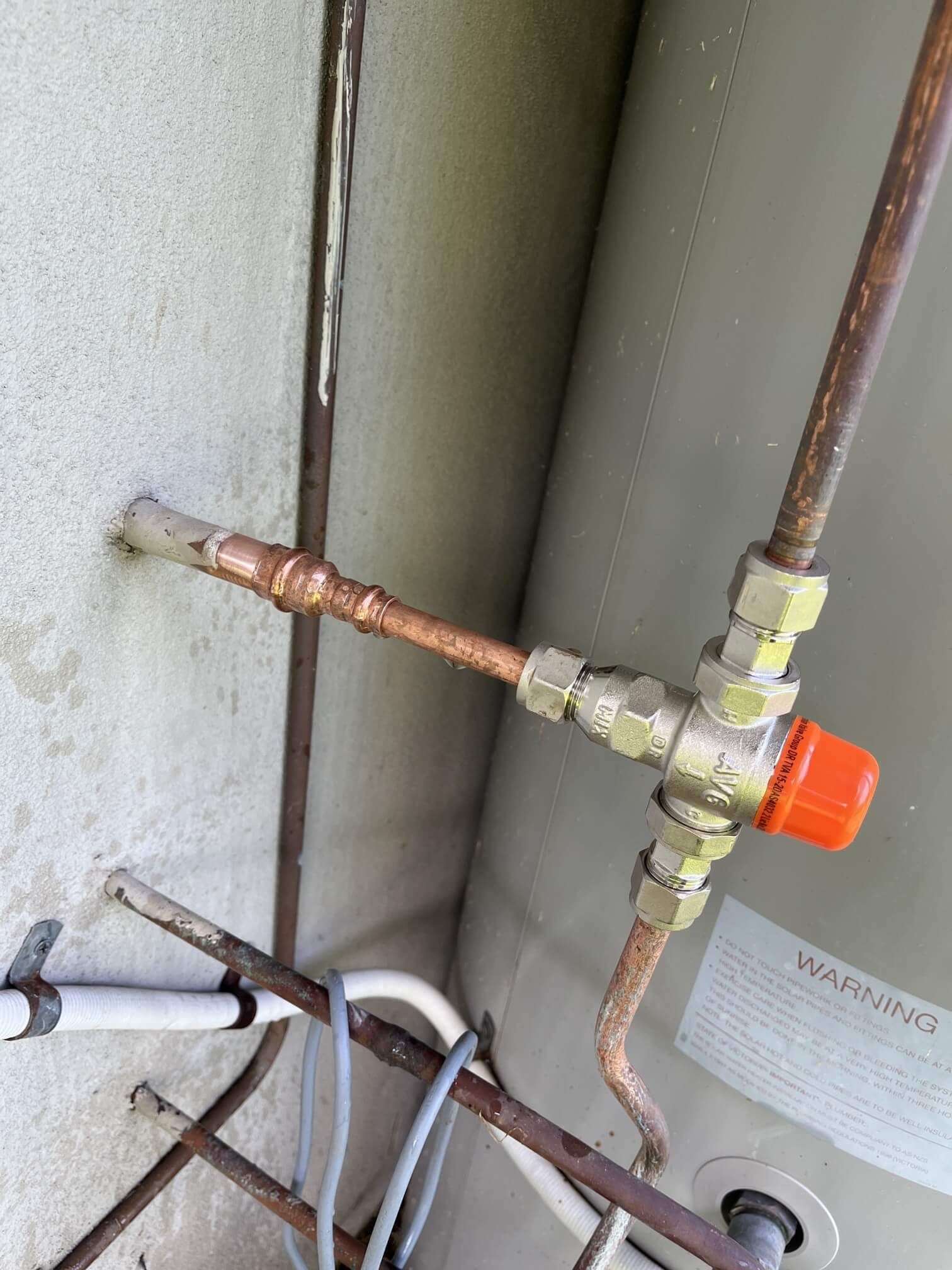 A close up of value of a water heater with copper pipes attached to it.