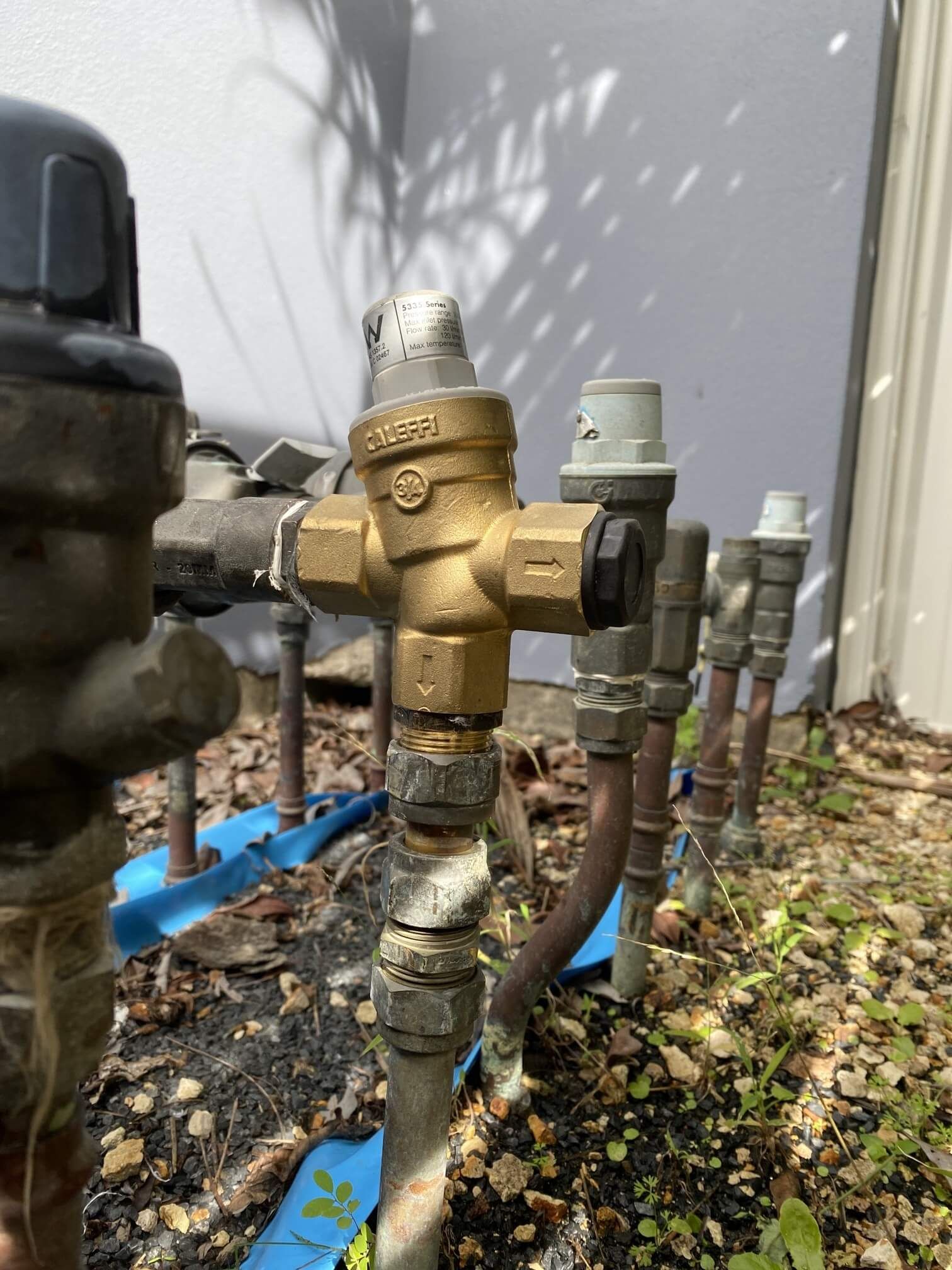 A row of outdoor irrigation valves, including a prominent brass-colored valve, installed on pipes in a garden area.