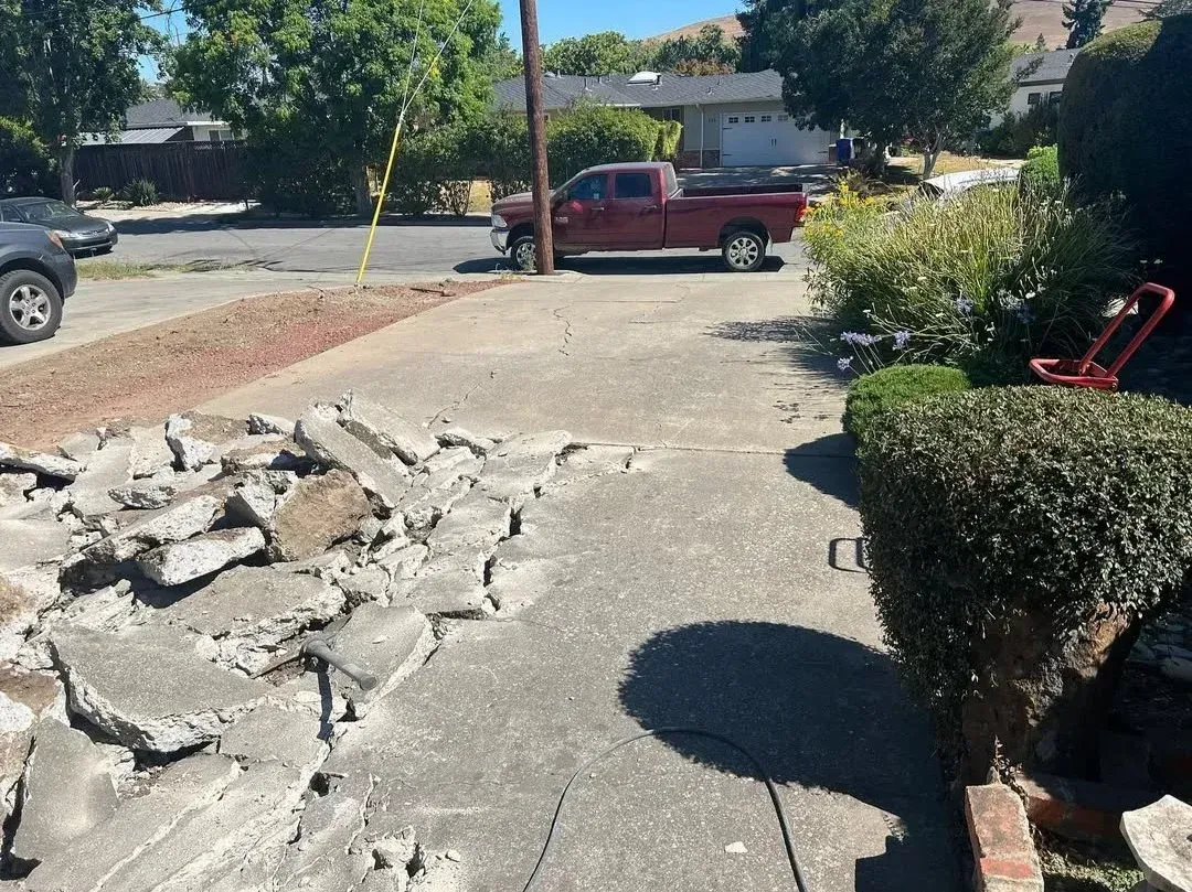 Cracked concrete driveway with rocks piled on the left and a red pickup truck parked in the background.