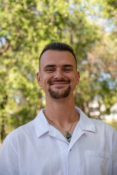 Portrait of a smiling man in a white shirt outdoors with blurred green trees in the background