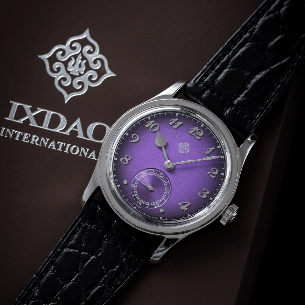 A silver watch with a purple face is sitting on a brown ixdaq international box