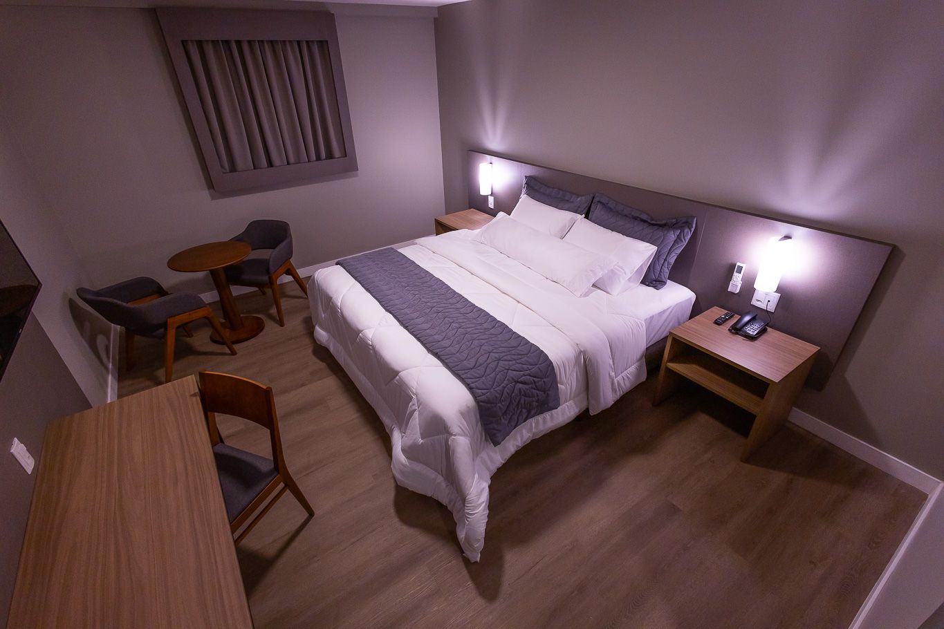 Quarto de hotel com cama, mesas de cabeceira, uma mesinha e cadeiras.