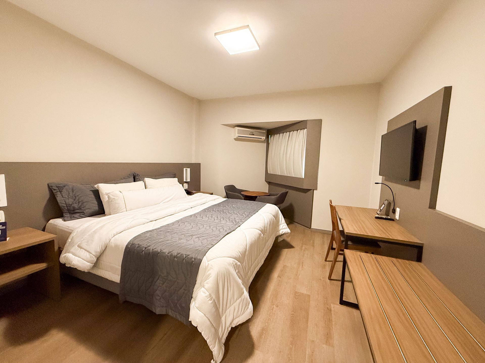 Quarto com cama king-size, porta de correr para o banheiro com azulejos vermelhos, dois abajures e obras de arte na parede.