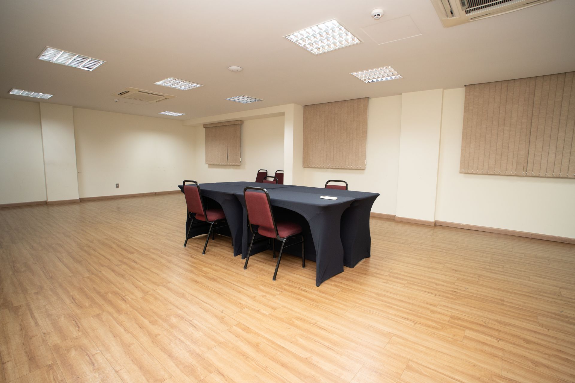 Sala de conferências com mesa e cadeiras em formato de U. Paredes e teto em tons claros.