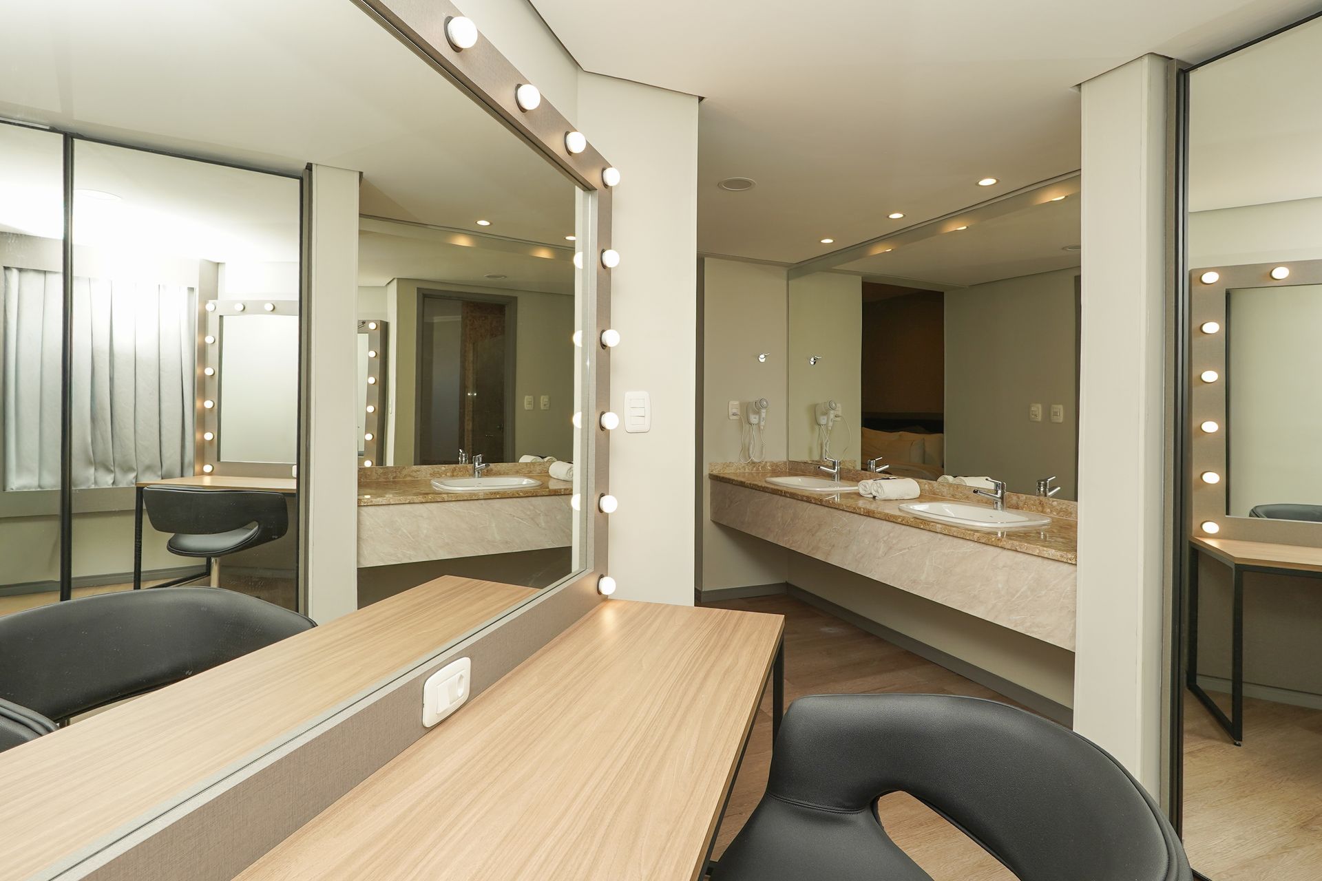 Closet moderno com espelhos, luminárias de camarim e bancos de madeira em um interior de tons neutros.