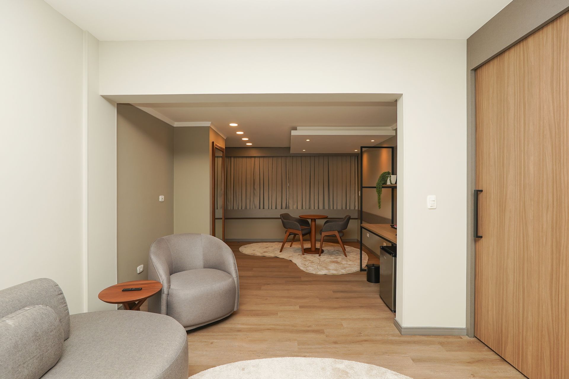 Sala de estar moderna com cadeiras cinza, piso de madeira e área de jantar além de uma porta ampla.