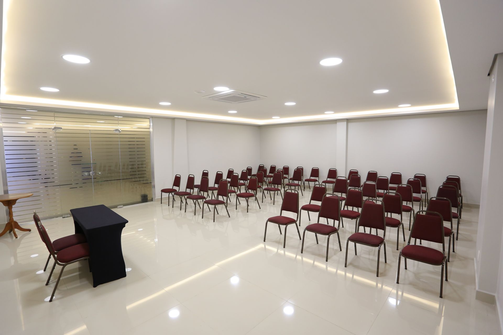 Quarto de hotel com três camas, uma escrivaninha e uma porta. Piso de madeira clara, paredes em tons neutros e peseiras bege.