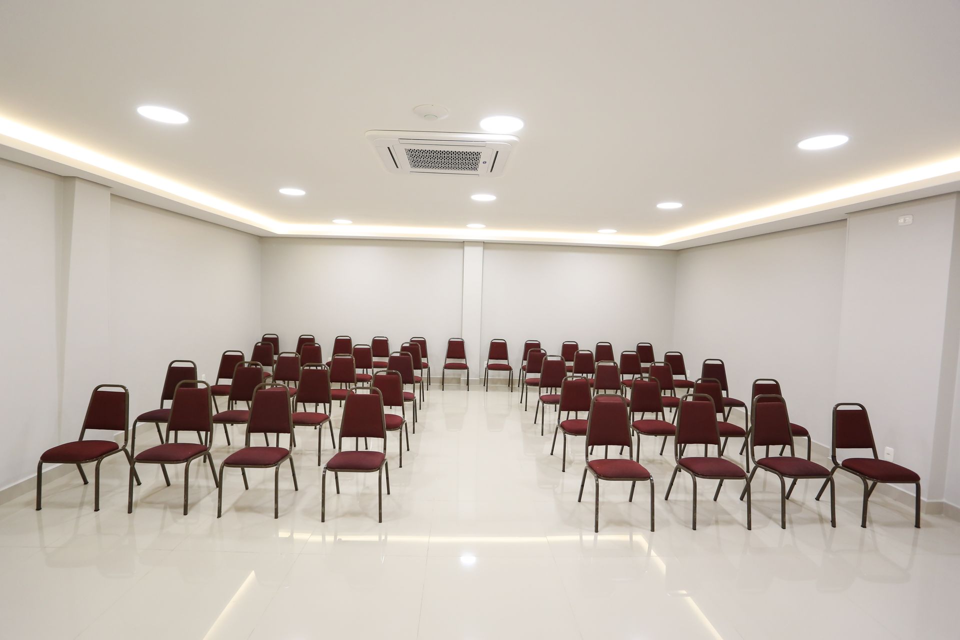Sala de conferências vazia com fileiras de mesas cobertas com toalhas pretas.